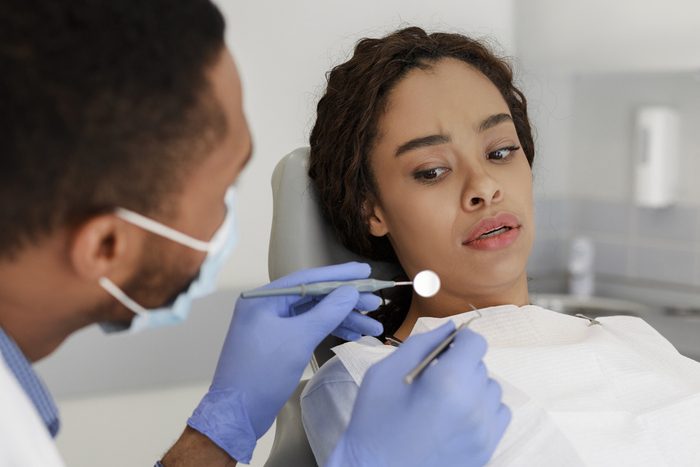 Scared black woman looking at dental tools in doctor hands