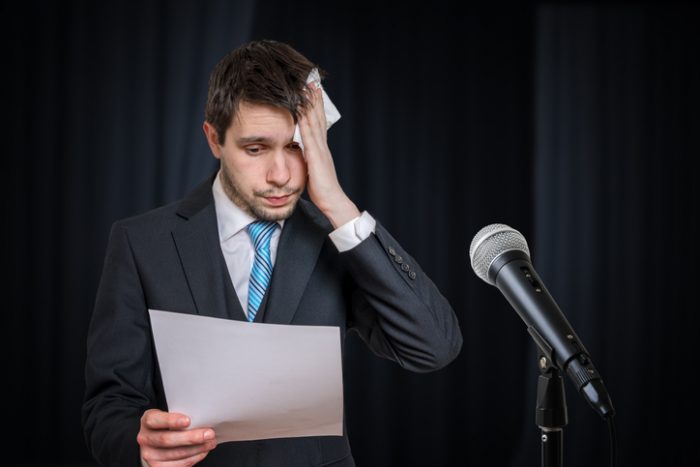 Sweating nervous speaker is afraid of public speech. Microphone in front.